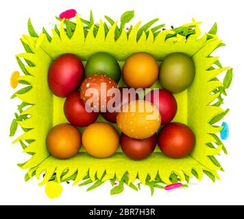 Stash of colorful Easter eggs, wax painted in a felt Easter basket on plain white background, isolated, top view Stock Photo