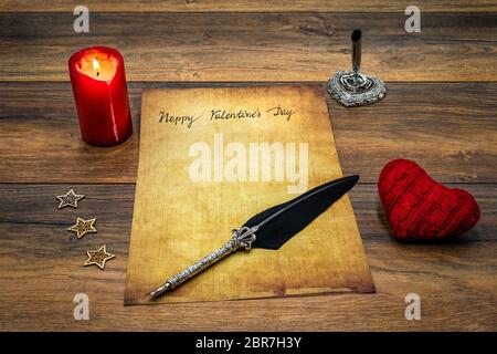 Antique preachment with hand written Happy Valentines Day, red lit candle, red cuddle heart, wooden decorations, detailed silver quill stand in shape Stock Photo