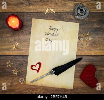 Antique preachment with hand written Happy Valentines Day, red lit candle, red cuddle heart, wooden decorations, detailed silver quill stand in shape Stock Photo