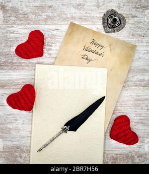 Antique preachment with hand written Happy Valentines Day, sticking out from book, 3 red cuddle heart, detailed silver quill stand in shape of hart, o Stock Photo