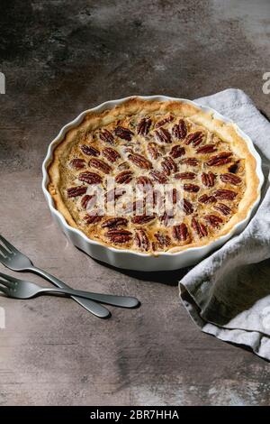 Fresh home baking classic american pecan caramel pie in white ceramic baking dish over grey texture background. Flat lay, space Stock Photo