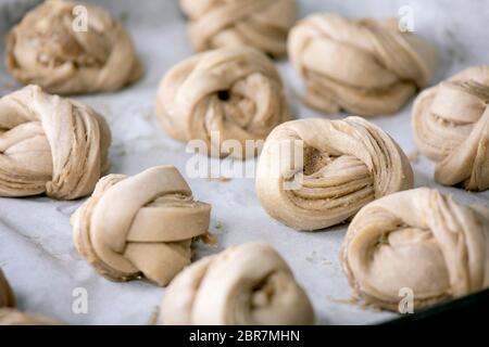 Ready to bake traditional Swedish cardamom sweet buns Kanelbulle on oven tray cover by baking paper. Stock Photo