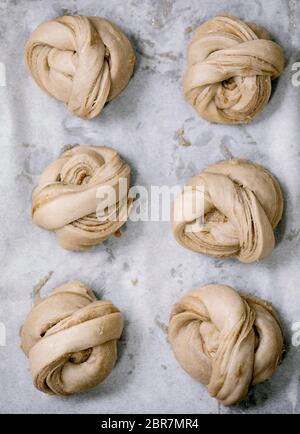 Ready to bake traditional Swedish cardamom sweet buns Kanelbulle on oven tray cover by baking paper. Flat lay, space Stock Photo
