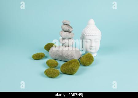 a pile of Zen stones in balance next to a Buddha's head surrounded by sparkling rocks on a turquoise summer background. Minimum color still life. Stock Photo