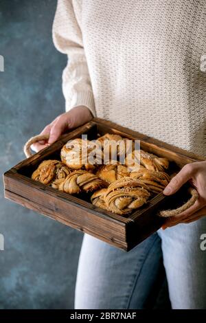 Woman in beige knitted sweater hold in hands wooden tray with home made traditional Swedish cardamom or cinnamon sweet buns Kanelbulle Stock Photo