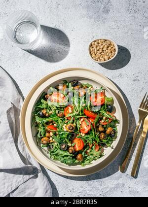 Salad with arugula, mini champignons, cherry tomatoes, black olives, pine nuts. Top view or flat lay. Copy space. Hard light. Vertical. Stock Photo