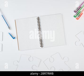 open notebook in a cell and on a white background, next to large blank puzzles, top view Stock Photo
