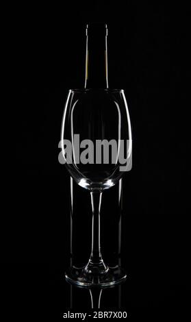 Empty wine glass in front of the wine bottle, isolated on black background. Stock Photo