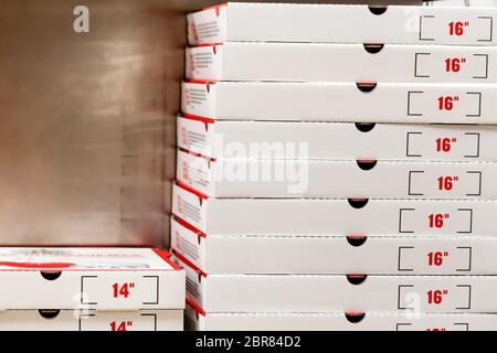 A large stack of white pizza boxes with red numbers diaimeter 16 Stock Photo