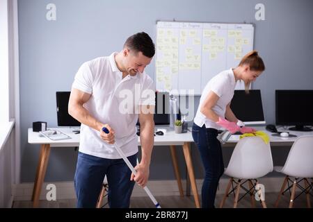 Two Smiling Young Janitor Cleaning The Desk And Mopping Floor In The Office Stock Photo