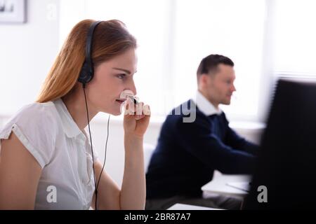 Side View Of Beautiful Female Telephone Operator Talking On Headphones At Workplace Stock Photo