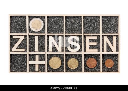 Plywood letters arranged in a collecting box with black decorative sand representing the word ZINSEN and euro coins a lying subjects in top view isola Stock Photo