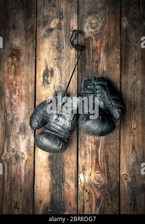 very old leather black boxing gloves hang on an old shabby wooden wall Stock Photo