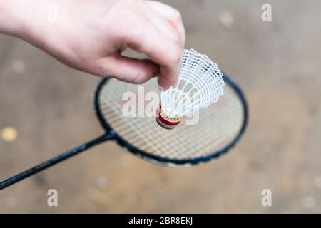 hand holds shuttlecock over badminton racquet on outdoor earth ground Stock Photo