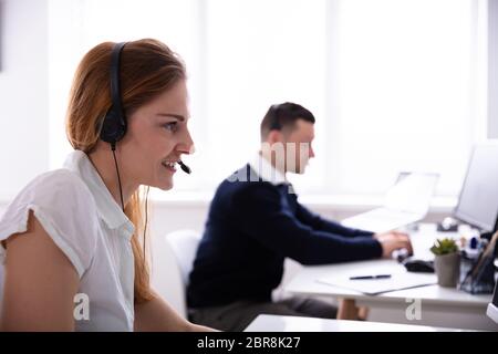Close-up Of Smiling Female Telephone Operator Talking On Headphones At Office Stock Photo