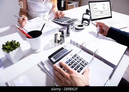 Elevated View Of Two Businesspeople Calculating Invoice With Calculator At Workplace Stock Photo