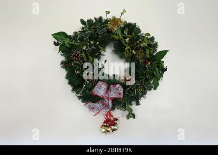 Home made Christmas wreath with holly, mistletoe, pine cones, ivy, tinsel, ribbon, artficial conifer twigs and bells against a light background with c Stock Photo