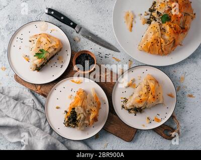 Greek pie spanakopita on gray background. Ideas and recipes for vegetarian or vegan Spanakopita Spinach Pie from fillo pastry. Slices pie on plates. C Stock Photo