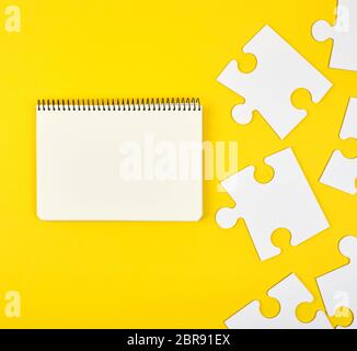 open notebook on a yellow background, next to large white blank puzzles, top view Stock Photo
