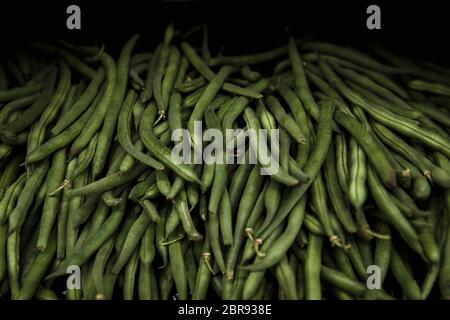 A close-up shot of an abundance of fresh green pea pods on display at a market stall.