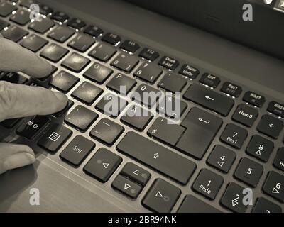 A lighted laptop keyboard, on the left side you can see three fingers pressing the buttons. A detail in a gentle black and white picture. Close Stock Photo