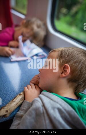 Little Caucasian boy and girl asleep inside the train carriage on their trip back home Stock Photo