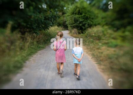 Brother and sister walking together on a narrow paved path in the countryside in summer Stock Photo
