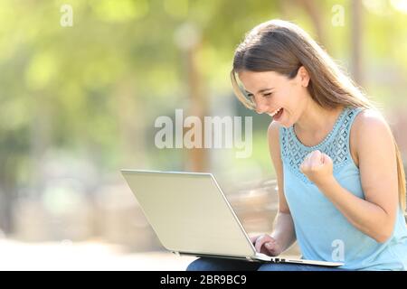 Excited woman checking laptop content celebrating good news in a park Stock Photo