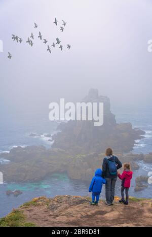 Mother with her children standing on the top of a cliff looking at the rock in the sea at the Lands End - the most westerly point of England, Penwith Stock Photo