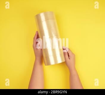 two female hands holding a stack of transparent scotch on a yellow background, adhesive tape Stock Photo