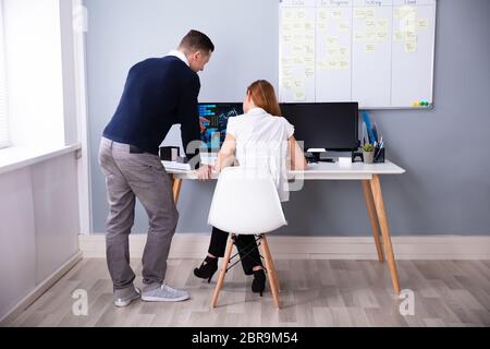 Rear View Of Two Businesspeople Analyzing Graph On Computer Screen In Office Stock Photo