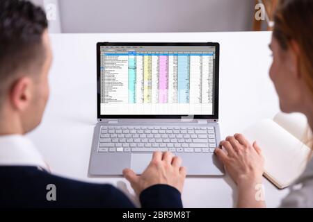 Male And Female Businesspeople Checking Spreadsheet On Laptop Screen Over Desk Stock Photo