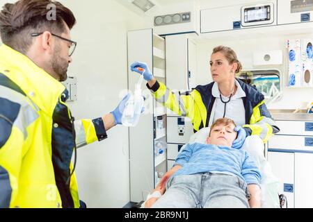Emergency doctor and paramedic giving infusion in ambulance to injured boy Stock Photo