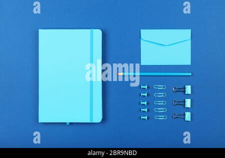 Neatly organized stationery flat lay of pastel blue notebook, envelope, pencil, office clips, binders and pins in order over dark indigo blue backgrou Stock Photo