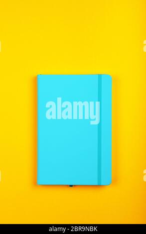 One closed blue faux leather cover notebook on vivid yellow paper background, flat lay, directly above Stock Photo