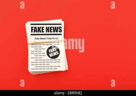 Close up stack of FAKE NEWS newspapers over red paper background with copy space, elevated top view, directly above Stock Photo