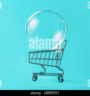 Shopping cart with soap bubble on bright blue background. Ephemeral happiness from shopping, shopaholism, consumerism concept. Shopping concept, minim Stock Photo