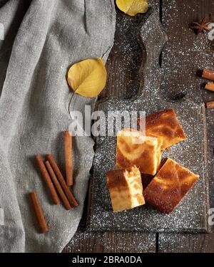 square slices of cottage cheese and pumpkin pie on a wooden board, dessert is sprinkled with icing sugar, top view Stock Photo