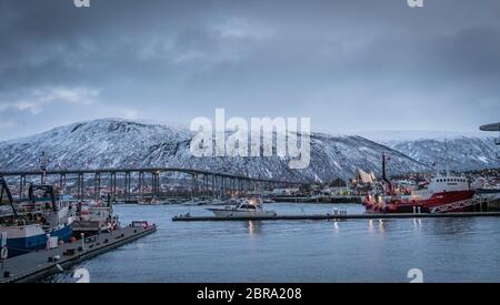Tromso, Norway -  December 2018 : Port and harbour with famous Tromso Bridge across Tromsoysundet strait in the background Stock Photo
