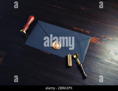 Retro postal stationery. Black envelope with golden wax seal, stamp and spoon on dark wooden background. Stock Photo