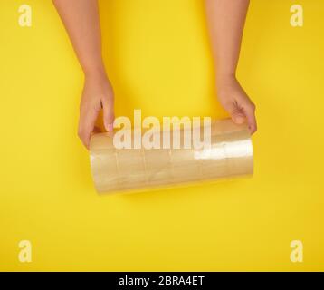 two female hands holding a stack of transparent scotch on a yellow background, adhesive tape Stock Photo