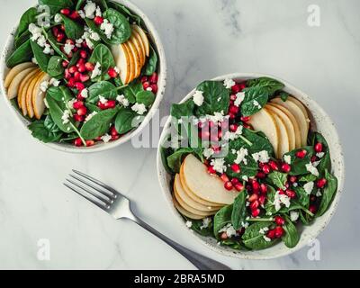 Fresh salad with baby spinach, pear, pomegranate and cottage cheese. Two bowls with delicious summer fruit salad on marble table. Copy space for text. Stock Photo