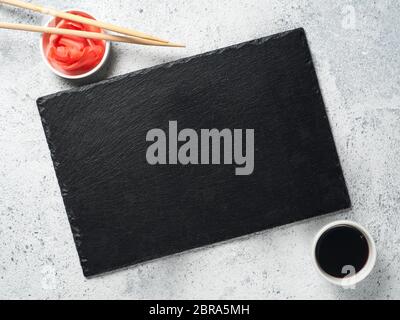 Empty slate plate on gray cement background with chopsticks, pickled ginger and soy sauce. Copy space. Top view or flat-lay. Concept for restaurant an Stock Photo