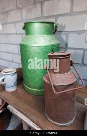 An old green tin can beside a rusted tin can on a shelf in front of white bricks wall. Stock Photo