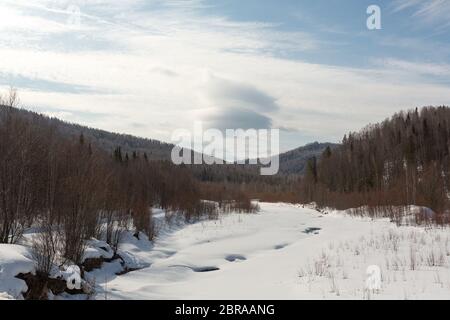 Frozen river in the forest covered with snow, in the background trees covered with snow, you can see the sky, the daytime beautiful nature Stock Photo