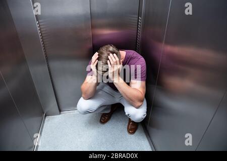Crouched Worried Man With Hands On Head In Elevator Stock Photo