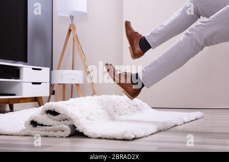 Low Section Of Man Legs Stumbling With A Carpet In The Living Room At Home Stock Photo