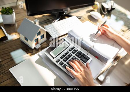 An Elevated View Of A Real Estate Agent Calculating Tax Over Wooden Table Stock Photo