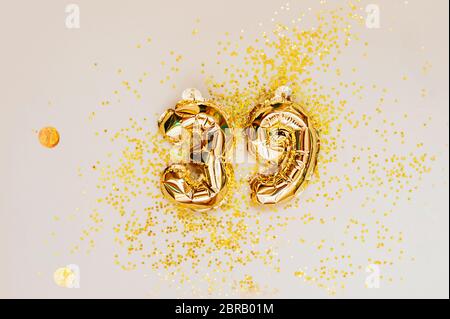 small foil gold balloons numbers 39 inflated with helium on a beige delicate background with gold sequins stars and balls. glittering holiday greeting Stock Photo