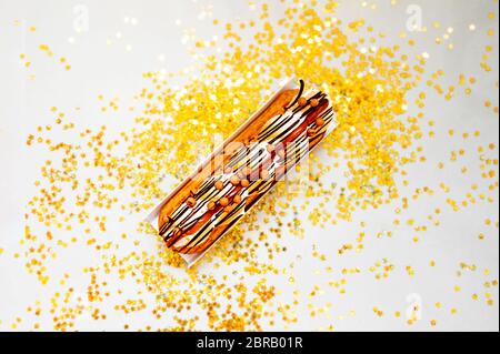 Caramel delicious fresh Eclair on a soft beige background with gold stars and sequins, top view, festive layout Stock Photo